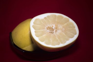 Kırmızı bir masa örtüsü üzerinde duran siyah bir plaka üzerinde pomelo yalan dilimlenmiş