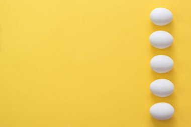 Sarı bir arka planda bir satırda Paskalya yumurtaları. Paskalya tatil yaratıcı tebrik kartı. Düz yatıyordu. Boşluk Kopyala. Üst görünüm