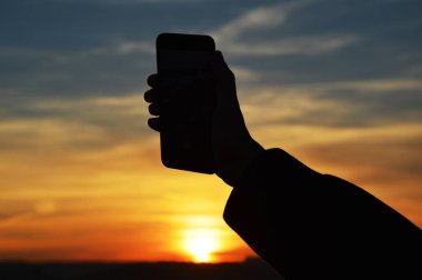Akıllı telefon günbatımında tutan erkek el