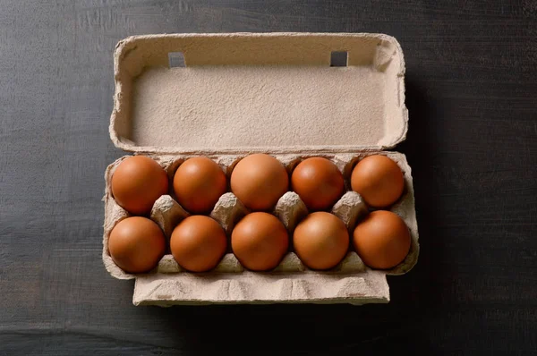 Brown eggs in a egg carton on black wood board