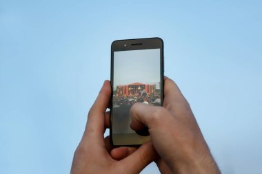 Cep telefonuyla el kaldırıldı. Açık hava konserinde fotoğraf çeken bir hayran. Arka planda bulanık sahne.