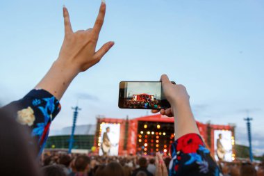 Rock konserinden hoşlanan fotoğrafçı kız, elini kaldırdı ve el çırptı, akıllı telefondan çekim yaptı.