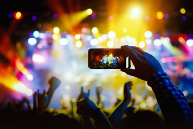 Canlı konserde fotoğraf ve video çekmek için telefon kamerasıyla el silueti.