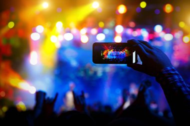 Konserde kalabalıktaki bir adam sosyal medyada yayınlanmış akıllı bir telefondan video kaydı ve resimler yapıyor.