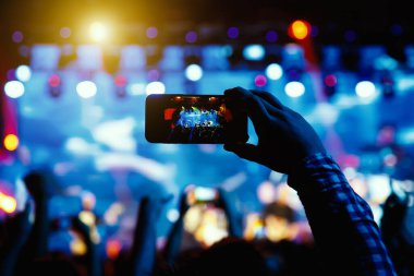 Canlı konserde fotoğraf ve video çekmek için telefon kamerasıyla el silueti.