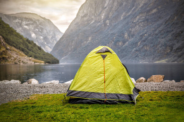 Camping tent at scenic wild fjord, a lake shore with mountain range in background - camping in Norway