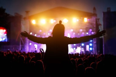 Elleri havada dans eden, şarkı söyleyen ve yaz müzik festivalinde konser sırasında müzik dinleyen kızlar.
