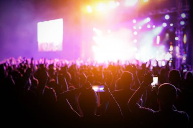 Parlak sahne ışıkları önünde konser kalabalığının siluetleri.