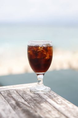 Masasında kola olan lale camı. Arka planda plaj şemsiyeleri