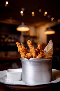 Metal bir tabakta aperatif olarak servis edilen kızarmış tavuk nuggetları ya da koyu bar arka planında parmak yiyeceği.
