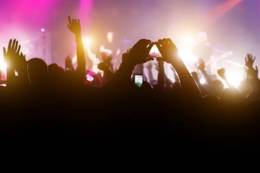Elleri havada ve akıllı telefonlardan oluşan kalabalık bir konser kaydediyor.