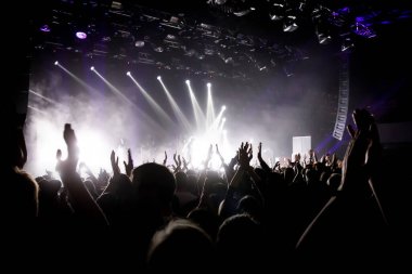 Müzik programındaki kalabalık, elleri havada mutlu insanlar. Beyaz sahne ışığı. Sahnede öncü