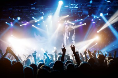 Işıklı bir konser salonu ve konser sırasında insanların siluetleri..
