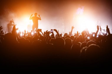 Rock konseri. Lider sahnede. Sahnenin önündeki kalabalığın silueti.