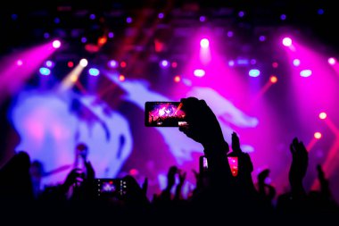 Konserde elinde akıllı telefon, sahneden gelen mor ışık..