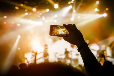 Cep telefonu kamerasıyla konser çekimleri, sahnenin sarı ışığı.