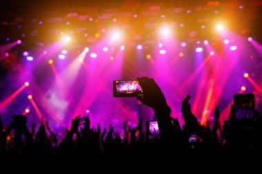 Konserde elinde akıllı telefon, sahneden gelen mor ışık..