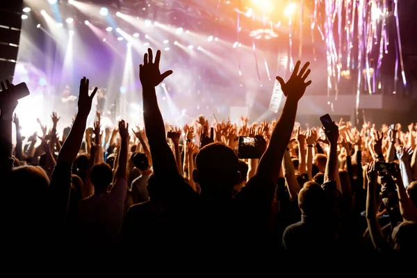 A man with his hands up at a concert of his favorite group. Light from the stage