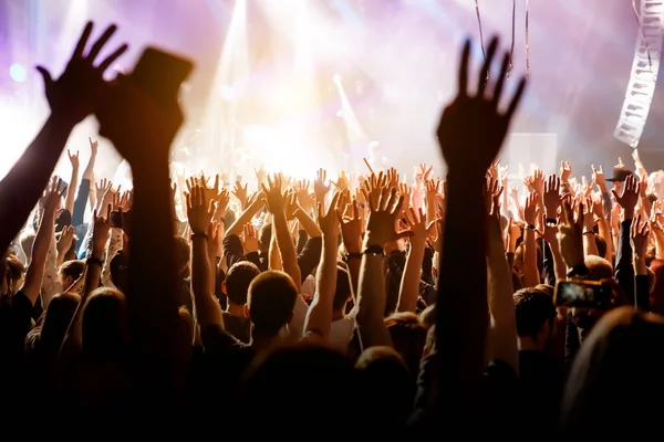 A man with his hands up at a concert of his favorite group. Light from the stage