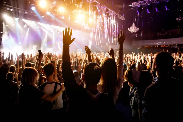 A man with his hands up at a concert of his favorite group. Light from the stage