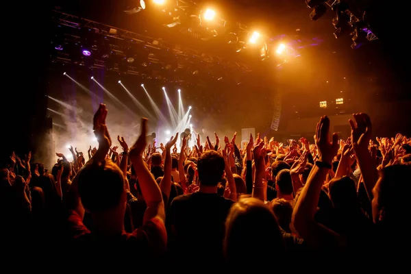 Crowd on music show, happy people with raised hands. Orange stage light