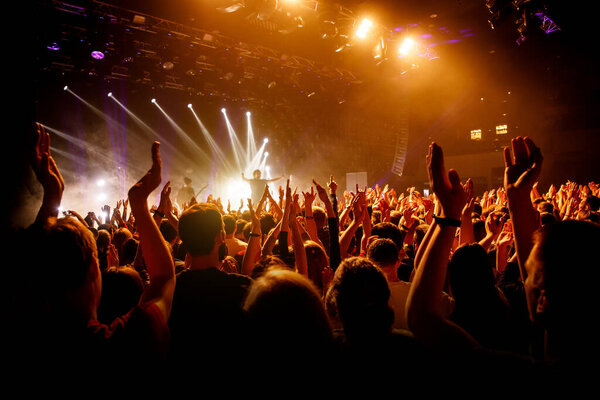 Crowd on music show, happy people with raised hands. Orange stage light