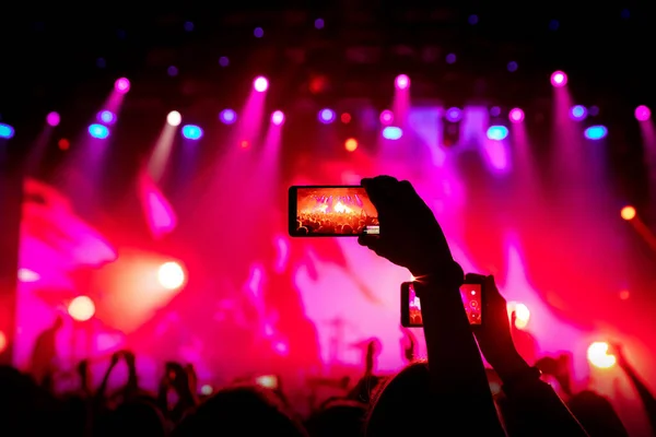 Smartphone in hand at a concert, red light from stage