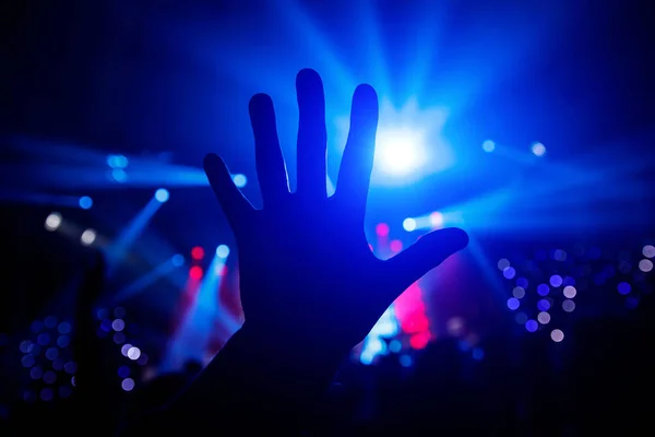 Black silhouette of the hand against the background of the concert scene. Five fingers
