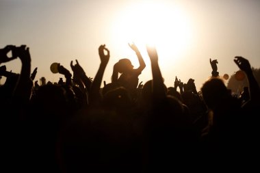 Kalabalık yaz müzik festivalinin, gün batımının, siyah siluetlerin, ortadaki kızın keyfini çıkarıyor.