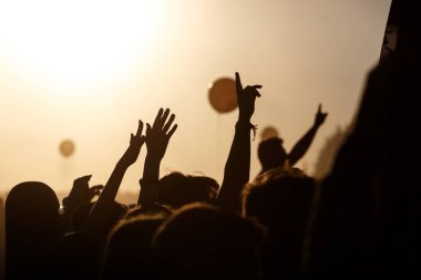 Mutlu insanların elleri kalabalık yazın sahnede eğleniyor Rock festivali, siyah siluetler, gün batımı