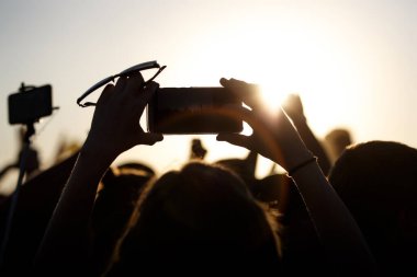 Yaz müzik festivali sırasında cep telefonuyla çekim yapmak. Kaldırılmış ellerin siyah silueti, günbatımı