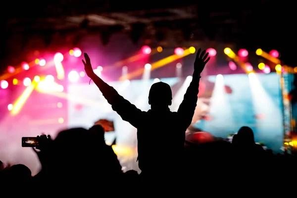 The crowd with their hands up enjoys music concert. Fan silhouette on stage background