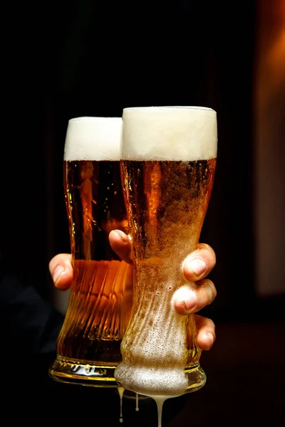 Two beer glasses with plentiful foam in hands