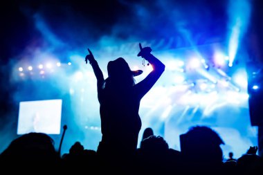 Müzik konserinde elini kaldırmış bir kız silueti..