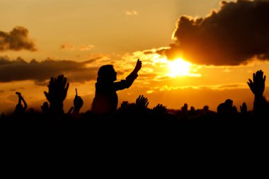 Gün batımına karşı kalabalığın üzerinde bir kız. Yaz festivalinde akıllı telefonunu kullanarak eğleniyor..