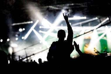 Konserde ellerini kaldırmış bir adamın silueti. Müzik programındaki kalabalık.