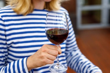 Çizgili yelekli kız elinde bir kadeh kırmızı şarap tutuyor..