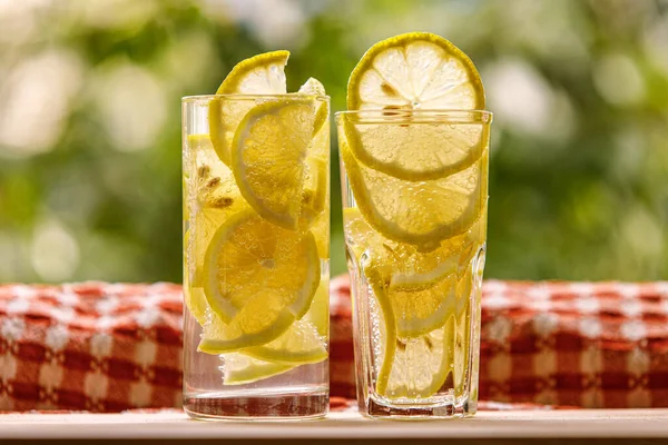 日当たりの良い庭の背景にレモンの水の眼鏡 — ストック写真