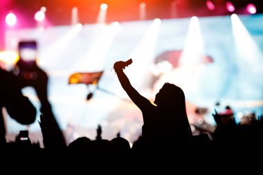 Müzik hayranı, sahnede ünlü bir sanatçının gece performansından zevk alıyor ve akıllı telefonunu kullanıyor.