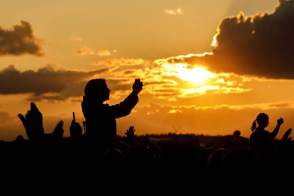 The young woman takes pictures of the festival on her smartphone. Black silhouette over sunset
