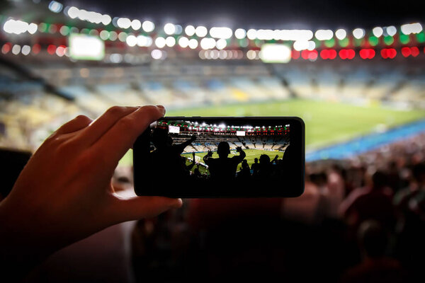 Taking pictures on a mobile phone in a sports stadium. Focused on fans