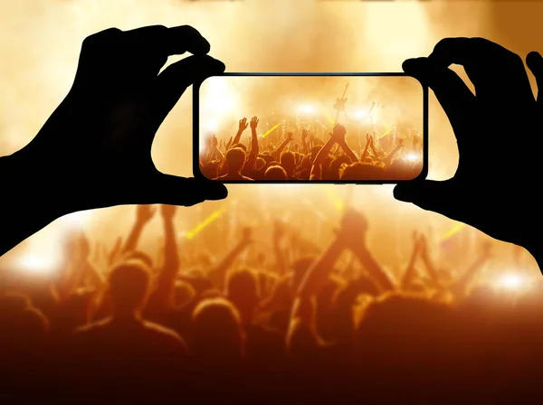 Silhouette of hand using camera phone to take pictures and videos at pop concert. Streaming to internet.