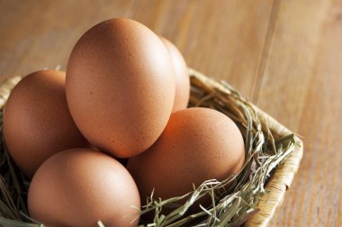 Beş kahverengi yumurta saman bir hasır sepet içinde yatıyordu. Sepeti ahşap bir masa üzerinde. Arka plan odağını. Yakın çekim.