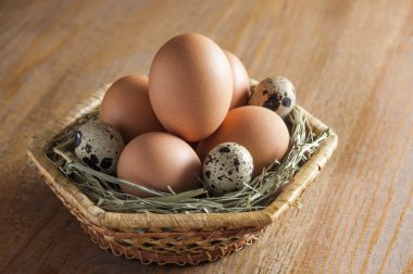 Tavuk ve Bıldırcın yumurta bir hasır sepet içinde saman üzerinde yalan. Ahşap bir masaya.