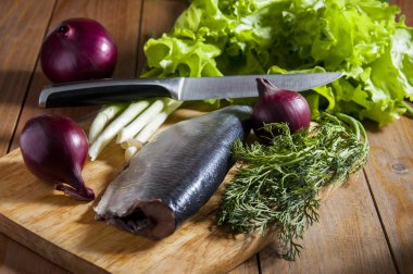 Kırmızı soğan, marul, dereotu ve ahşap kesme tahtası üzerinde chives ile ringa balığı.