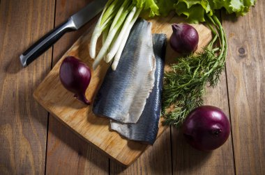 Kırmızı soğan, frenk soğanı, marul ve dereotu ahşap kesme tahtası ile ringa balığı.
