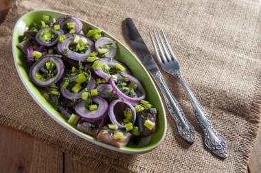Dilimleri altında kırmızı soğan ve bıçak ve çatal çuval bezi üzerinde ringa balığı filetosu. Yakın çekim.