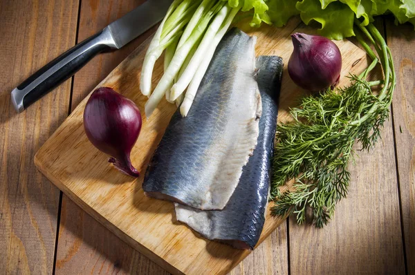 Kırmızı soğan, frenk soğanı, marul ve dereotu ahşap kesme tahtası ile ringa balığı. Ahşap masa üzerinde çevre bıçak.