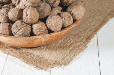 Birçok ceviz bir kase. Çuval bezi üzerinde top. Beyaz ahşap zemin. 