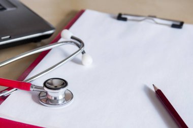 Masadaki kırmızı panoda kırmızı steteskop ve kırmızı kalem. Ne?